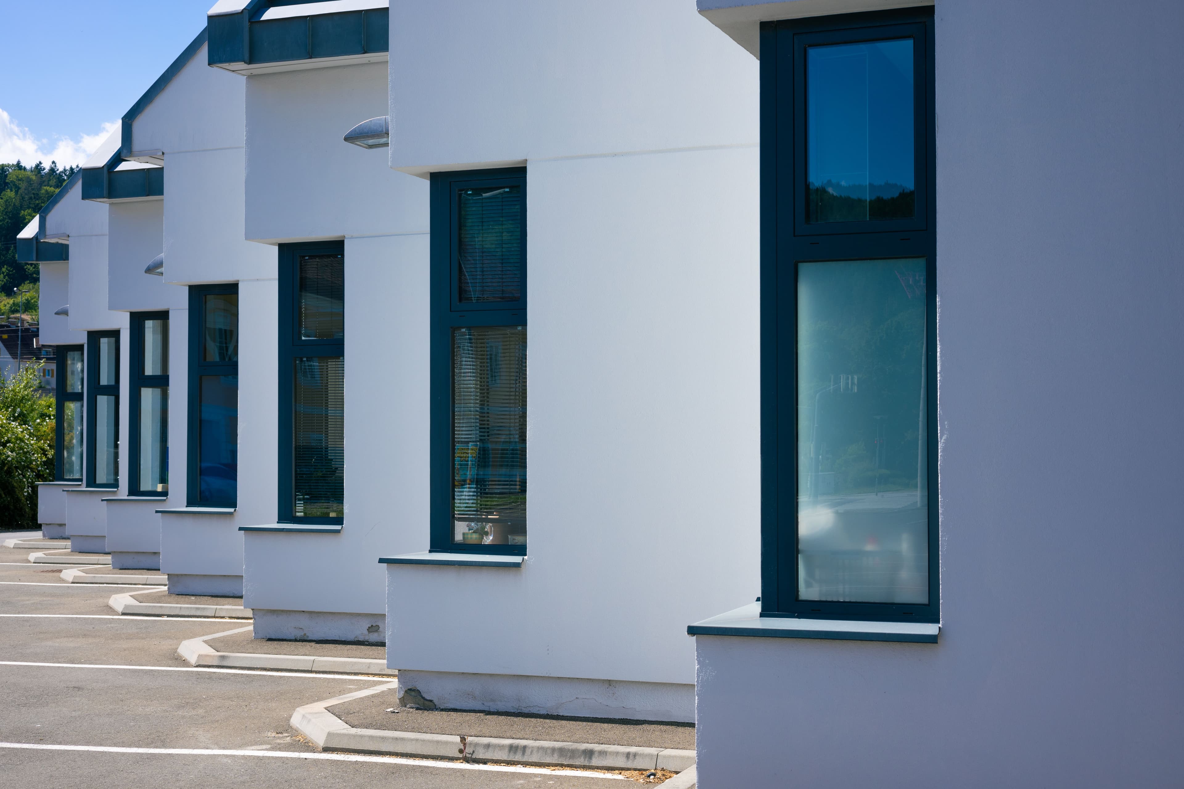 Modern white buildings with dark-framed windows receding in perspective under a bright blue sky.